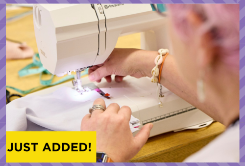 a pink haired lady feeds fabric through her sewing machine