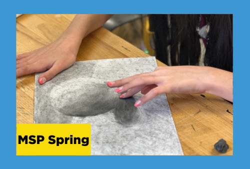 A close-up of charcoal hands smudging the drawing of an apple