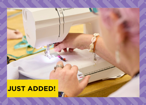 a pink haired lady feeds fabric through her sewing machine