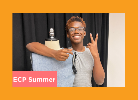 a student throws up a piece sign next to their fabric draped on a dress form